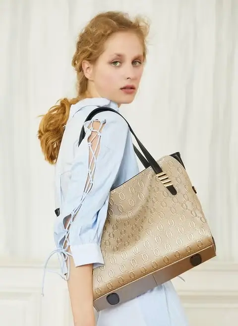 Woman in a light blue blouse carrying a gold-tone Boyatu tote bag on her shoulder