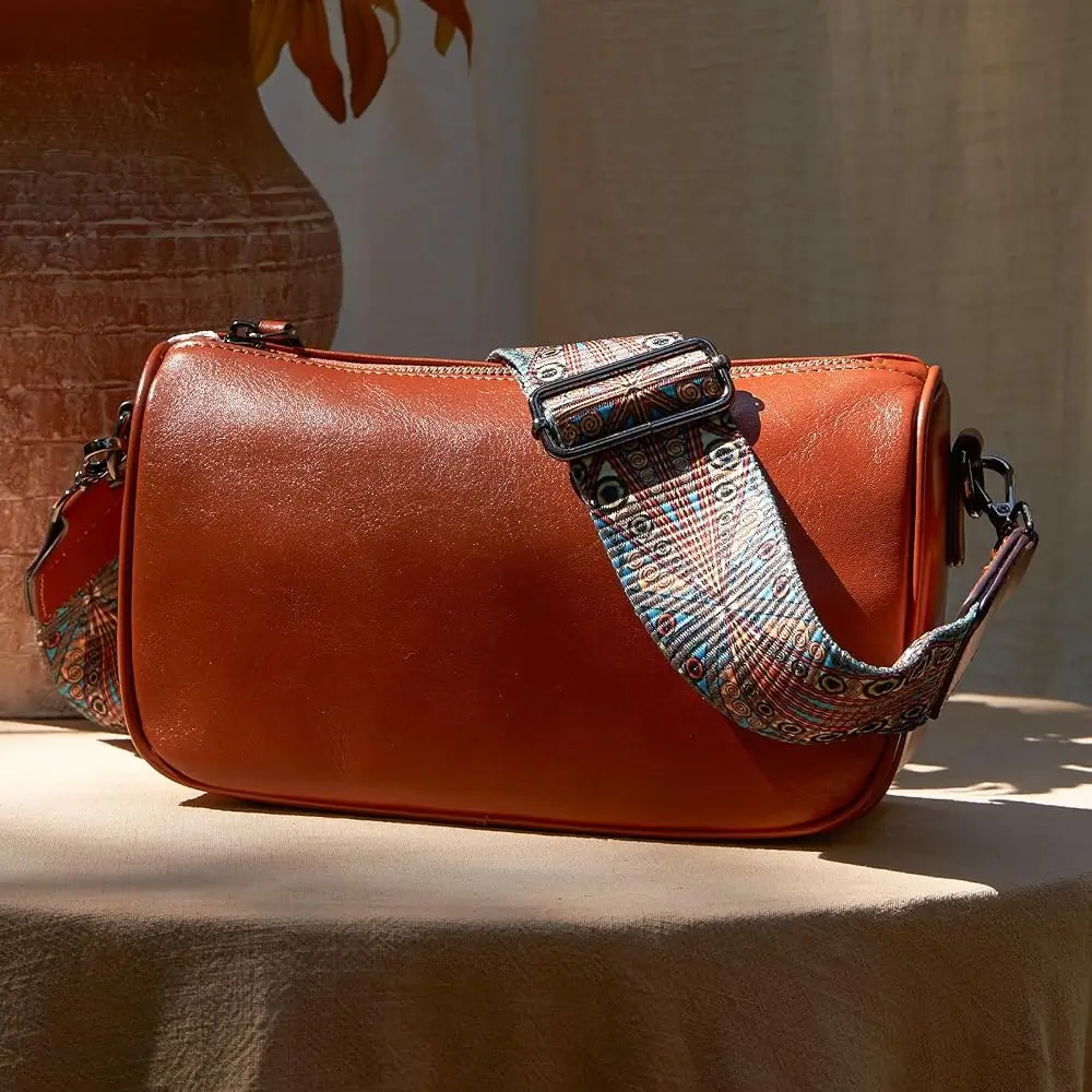 Cognac leather Boyatu crossbody bag with a woven patterned strap resting on a linen-covered table