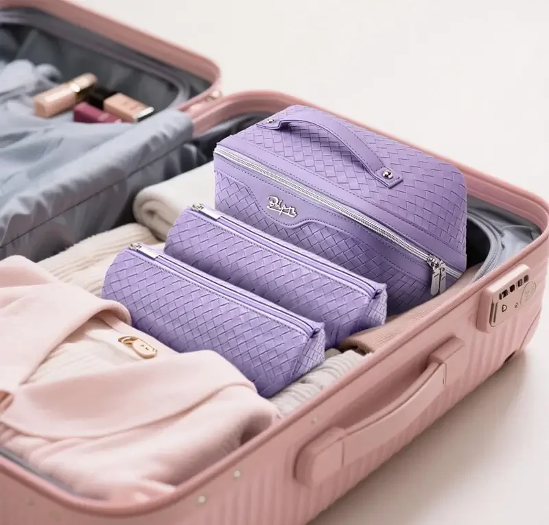 Three lavender woven Boyatu makeup bags packed inside an open pink suitcase